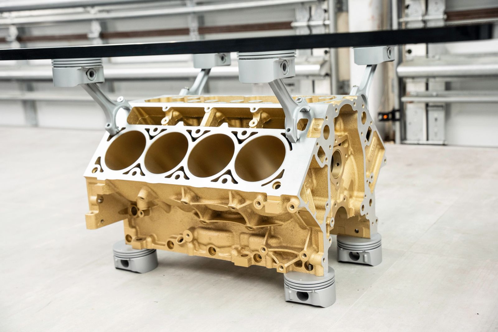 Bare V8 engine block finished in satin gold on piston feet under glass